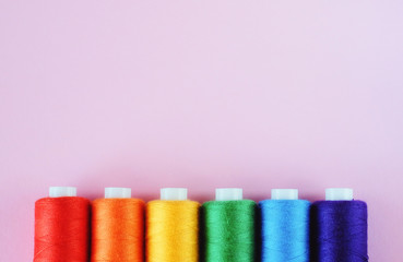 LGBT flag colors creative concept. Rainbow color sewing treads on the pink pastel  background with the empty space for text. Sewing accessories.