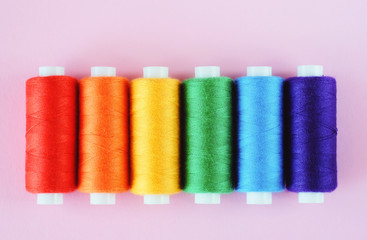 LGBT flag colors creative concept. Rainbow color sewing treads on the pink pastel  background.