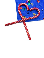 Fototapeta premium Happy holidays greeting card with striped candy canes in a heart shape with a colorful stars on trendy blue background with copy space. Birthday, Valentines day, Christmas, New Year. Flat lay