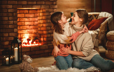 family mother and child reading book and drink tea on winter evening by fireplace