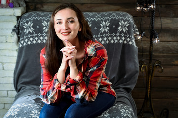 Fototapeta premium The concept of home comfort. Photo of a pretty young brunette woman with good make-up sits on a sofa in the home interior. Smiling happy.