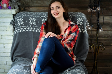 The concept of home comfort. Photo of a pretty young brunette woman with good make-up sits on a sofa in the home interior. Smiling happy.