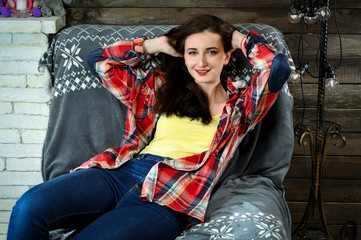 Photo of a pretty young brunette woman with good make-up sits on a sofa in the home interior. The concept of home comfort. Smiling happy.