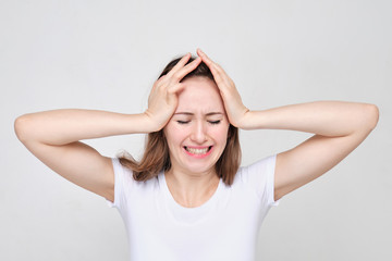Fototapeta premium A girl in a white T-shirt holds head with her hands. The concept of stress and problems.