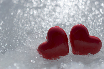Fototapeta premium Two hearts in the snow. Valentine's Day and February 14th concept. A pair of red hearts in the sparkling snow. Winter picture about love. Template for a greeting card. Background, copy space