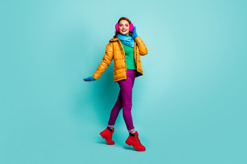 Full body photo of content candid woman enjoy winter autumn weekend go walk touch ear warmers wear pink red bright boots isolated over teal color background