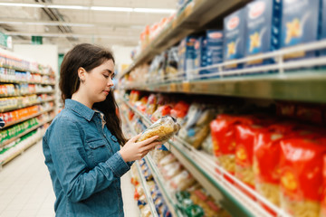 Shopping at the grocery store. A young woman in a denim shirt reads the information on a packet of...