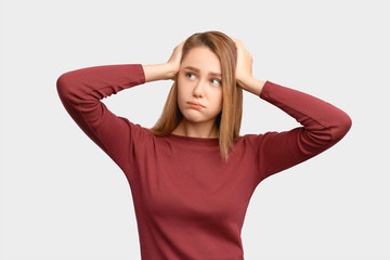 Sad girl puffs out cheeks because of resentment keeps hands on head, does not want to hear anything. Beautiful young woman isolated on background in Studio with an empty space for text and advertising