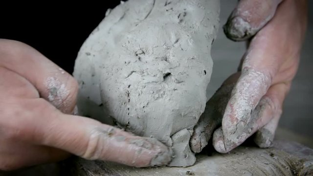 Sculptor creates a bust and puts his hands clay on the skeleton of the sculpture. Close-up