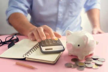 A hand counting on calculator closeup for expense list with money coin and piggy bank. A saving...