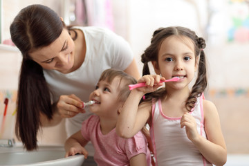Happy family mom and her kids in bathroom. Mom teaches teeth brushing her younger daughter