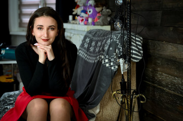 Fototapeta na wymiar Model in a dark blouse and a red skirt. Photo of a pretty young brunette woman with good make-up sits on a sofa in the home interior. The concept of home comfort. Smiling happy.