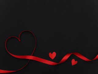 Red ribbon in heart shape on black background with copyspace for valentine day greeting card.