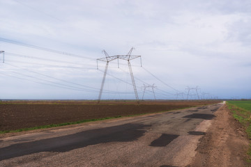Rural landscape. Bad stretch of road through a field with electric power lines