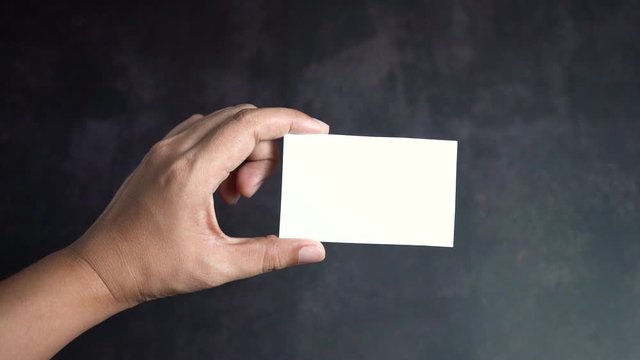 Hand holding mockup white business card on black background, Slow motion.