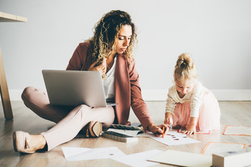 Businesswoman working on laptop while coloring with daughter