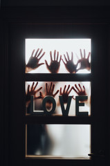 Word - LOVE. Hands and fingers of people in silhouette against the background of a door with a window, locked and asking for help. Horror. Swingers, group sex, swedish family, relax and orgy concept.