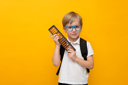 Cute little school boy in glasses holding abacus on yellow background. Mental arithmetic