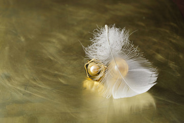 Vintage cufflinks with artificial  pearls and a white heron feather on a gold mirror surface. Copy space.