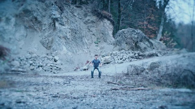 Person powering up into super power form 4K. Wide static shot of a man in focus doing a flexing muscles making an energy aura. No audio.
