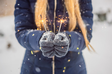 Sparklers in female hands on a background of snowfall. Christmas and New Year concept