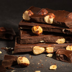 Pieces of chocolate with a nuts   lying on a dark texture table.