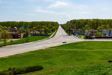 paved road with markings and road signs, passing among houses and forests