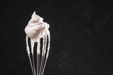 Close up of a hand balloon whisk with beaten egg white raw meringue for perfect peaks on black...