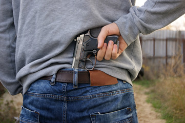 A man in jeans and a sweatshirt holds a gun in his hand from the back.
