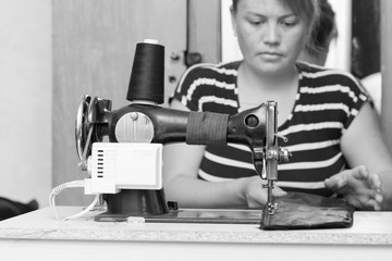 Pretty female tailor sits at table with sewing machine and sews fabric.