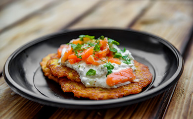 potato pancakes withsalmon fish and sour cream in a plate on wooden table