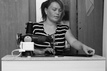 Pretty female tailor sits at table with sewing machine and sews fabric.
