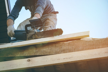 Worker is sawing a wooden balk on the house roof close up.