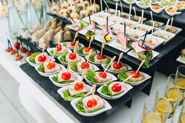 Buffet reception of different delicious food at a wedding celebration. Snacks for guests. Wedding party. Canapes, sushi, fruit, meat, drink, wine, juice.