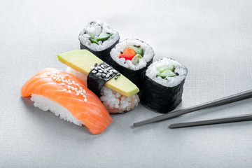 Set of Sushi nigiri with salmon and avocado, and rolls with cucumber on a gray background with chopsticks, traditional Japanese food concept