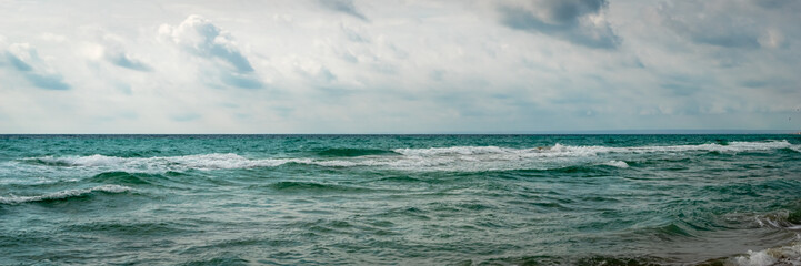 Panorama of big stormy waves on the coast. Dramatic sky background. Skyline, horizon. Amazing view of grey rainy clouds in the ocean. Header.