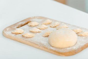 selective focus of flour near raw dumplings on wooden chopping board