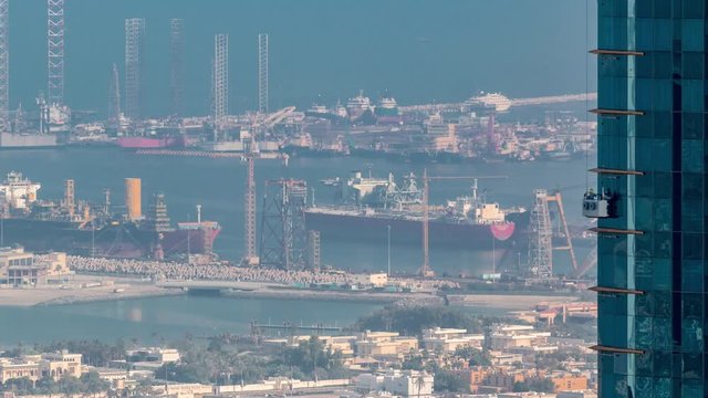 Aerial morning view from Downtown of Dubai timelapse with windows cleaners on skyscraper, houses and port Rashid on a background, ships docking at sea port, UAE