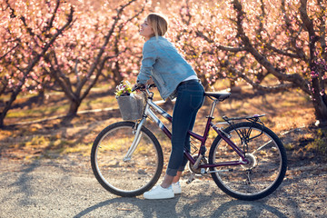 Pretty young woman with a vintage bike looking the cherry blossoms on the field in springtime.