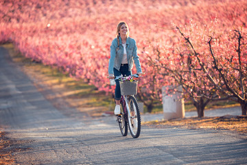 Pretty young woman riding with a bike in cherry field in springtime.