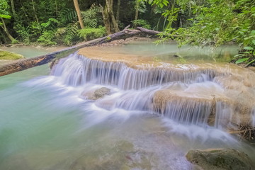 Beautiful silky water cascade flowing on cliff rocks around with blue-green water and green forest background, Erawan Waterfalls, 1th step, Kanchanaburi, west of Thailand.