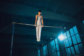 Little male gymnast training in gym, flexible and active. Caucasian fit little boy, athlete in white sportswear practicing in exercises for strength, balance. Movement, action, motion, dynamic concept