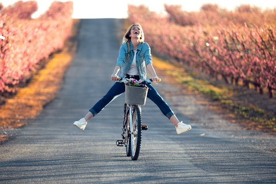 Pretty young woman with a vintage bike enjoying the time in cherry field in springtime.