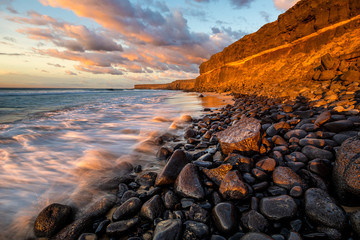 Beautiful sunset at the ocean beach under a rocky cliff, cliff coast south of El Cotillo, Canary...