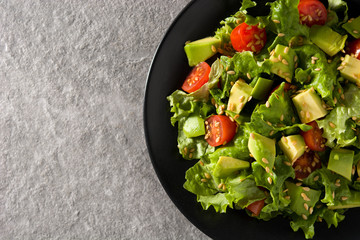 Salad with avocado, lettuce, tomato and flax seeds on gray background. Top view. Copy space	