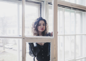 Glamorous young woman in black leather jacket and in windows