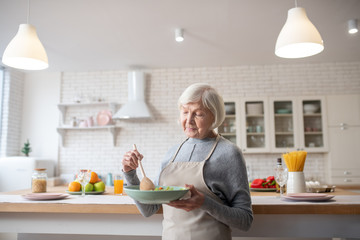 Grandmother standing in the kitchen with a vegetable salad.