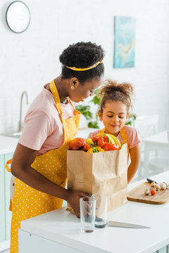 Attractive African American Mother And Daughter Looking At Paper Bag With Groceries