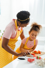 african american mother looking at smiling daughter in kitchen