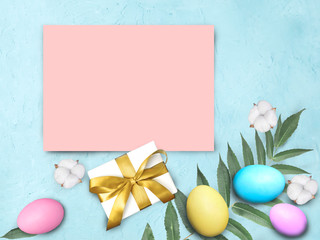 Mock up Easter composition  with empty pink blank, colorful eggs, cotton flowers and gift box on blue background. Greeting holiday flat lay with copy space.